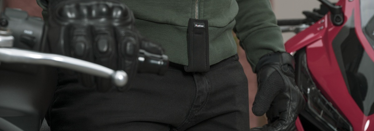 A close-up view of a motorcycle tank with a high-quality zipper cover called "ZipCov" installed, designed to prevent scratches. The foreground features the textured fabric of the zipper cover, showcasing its intricate stitching and protective features. In the middle, the sleek motorcycle tank is visible, reflecting a polished metallic surface with subtle reflections of light. The background is blurred, hinting at an outdoor setting with soft natural lighting, creating an inviting atmosphere. The overall mood should convey a sense of protection and style, highlighting the functionality of the zipper cover without distractions. Use a slight overhead angle to emphasize the details of the zipper cover and the tank's surface.